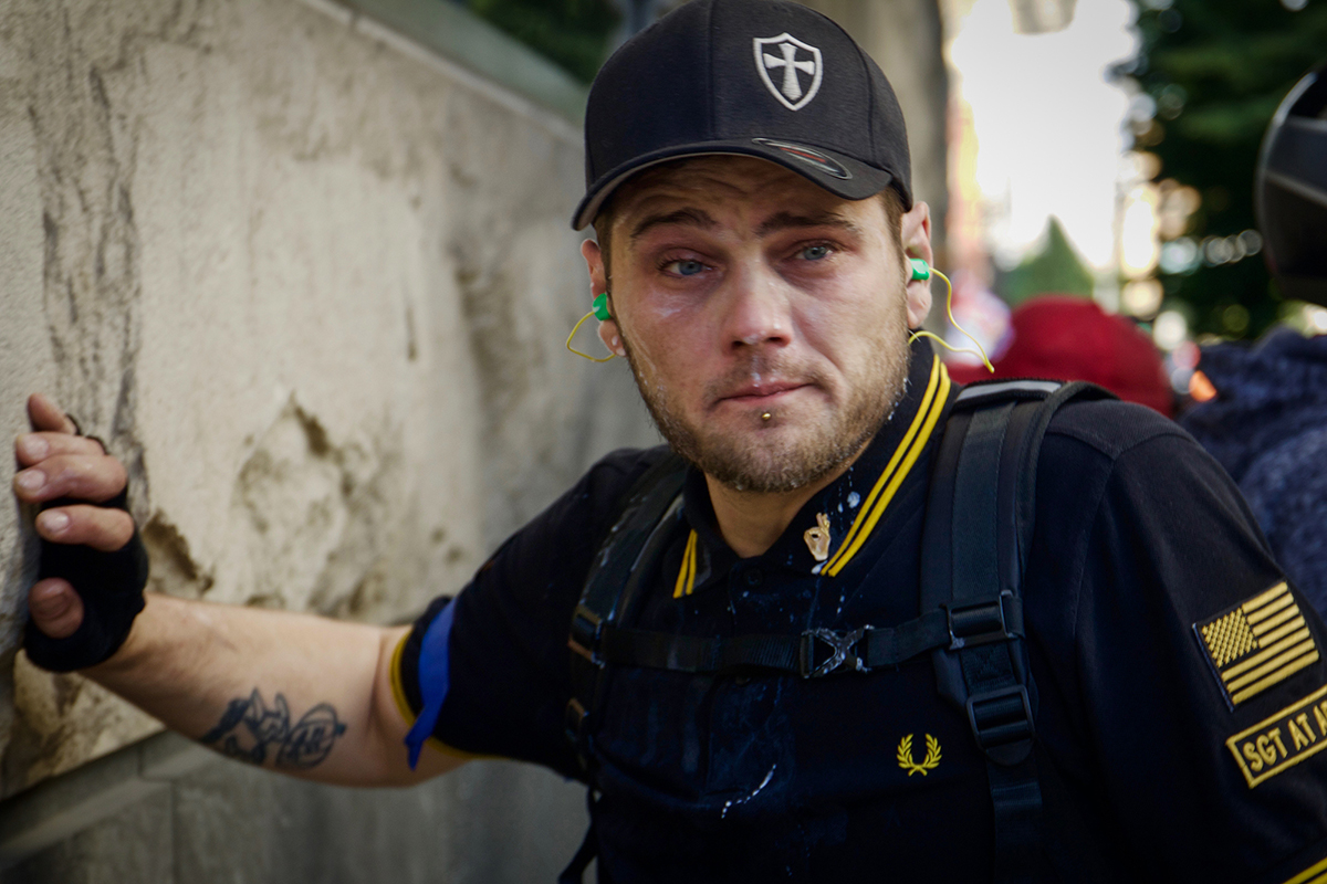 A Proud Boy who was pepper-sprayed recovers after pouring milk over his face. His ears were jammed with plugs to try and protect against the sound canons used by police to disperse the crowd. (Rosanna Cooney/News21)
